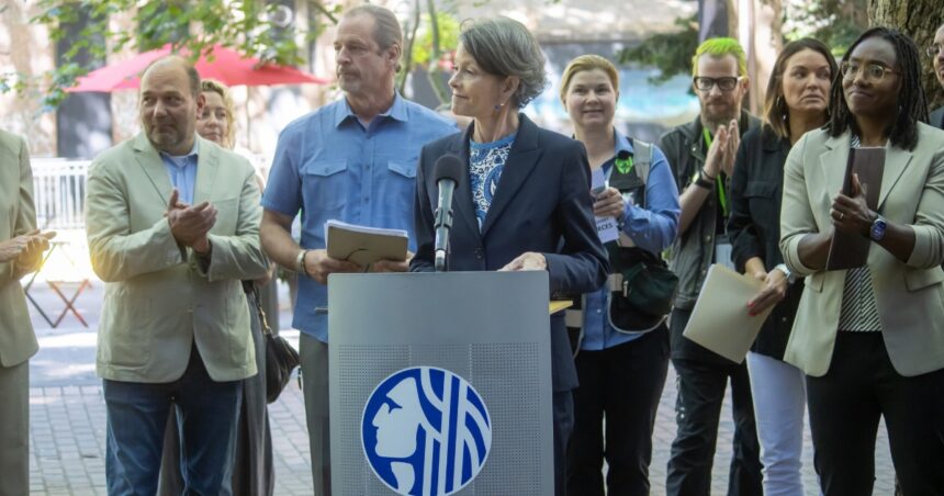 Council President Sara Nelson speaking at a podium in Occidental Square Park, surrounded by clapping supporters of her new legislations