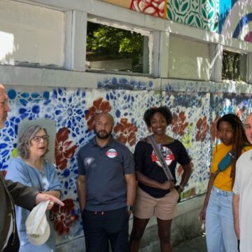 a diverse group standing in front of a street mural, having a discussion